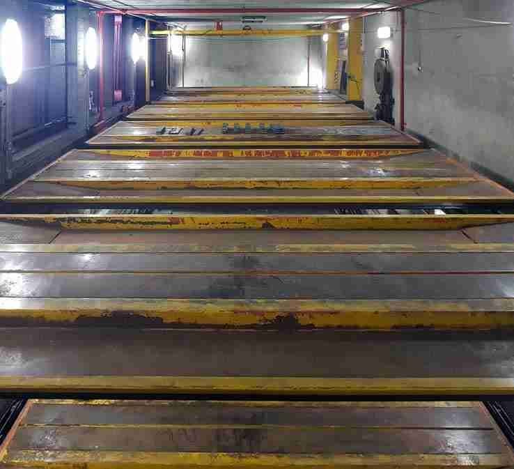 Interno parcheggio automatico prima della ristrutturazione - piattaforme gialle e rosse arrugginite, pareti sporche, illuminazione scarsa